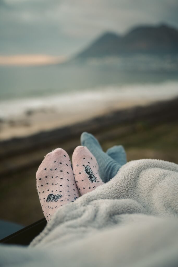 Pieds en chaussettes roses et bleues sous une couverture douce, face à la mer.